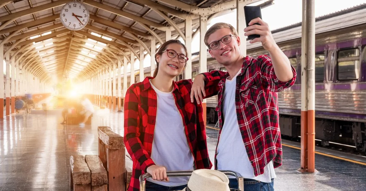 Jeune couple prenant un selfie sur un quai de gare urbaine.