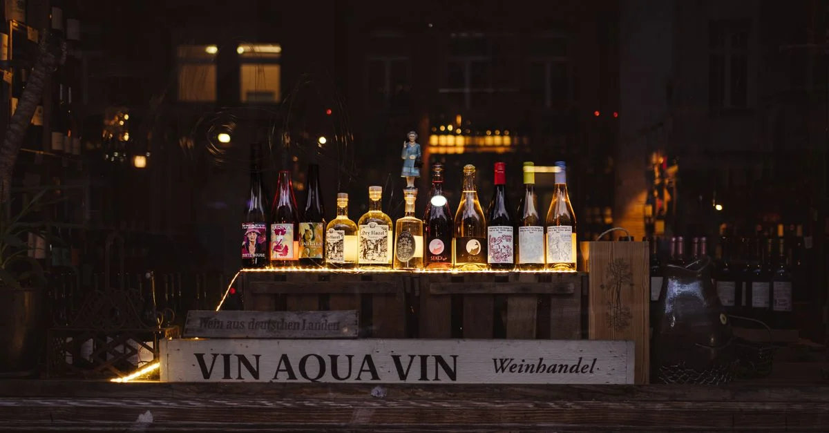 Une vitrine nocturne présentant une variété de bouteilles de vin et de spiritueux illuminées dans une mise en scène élégante.
